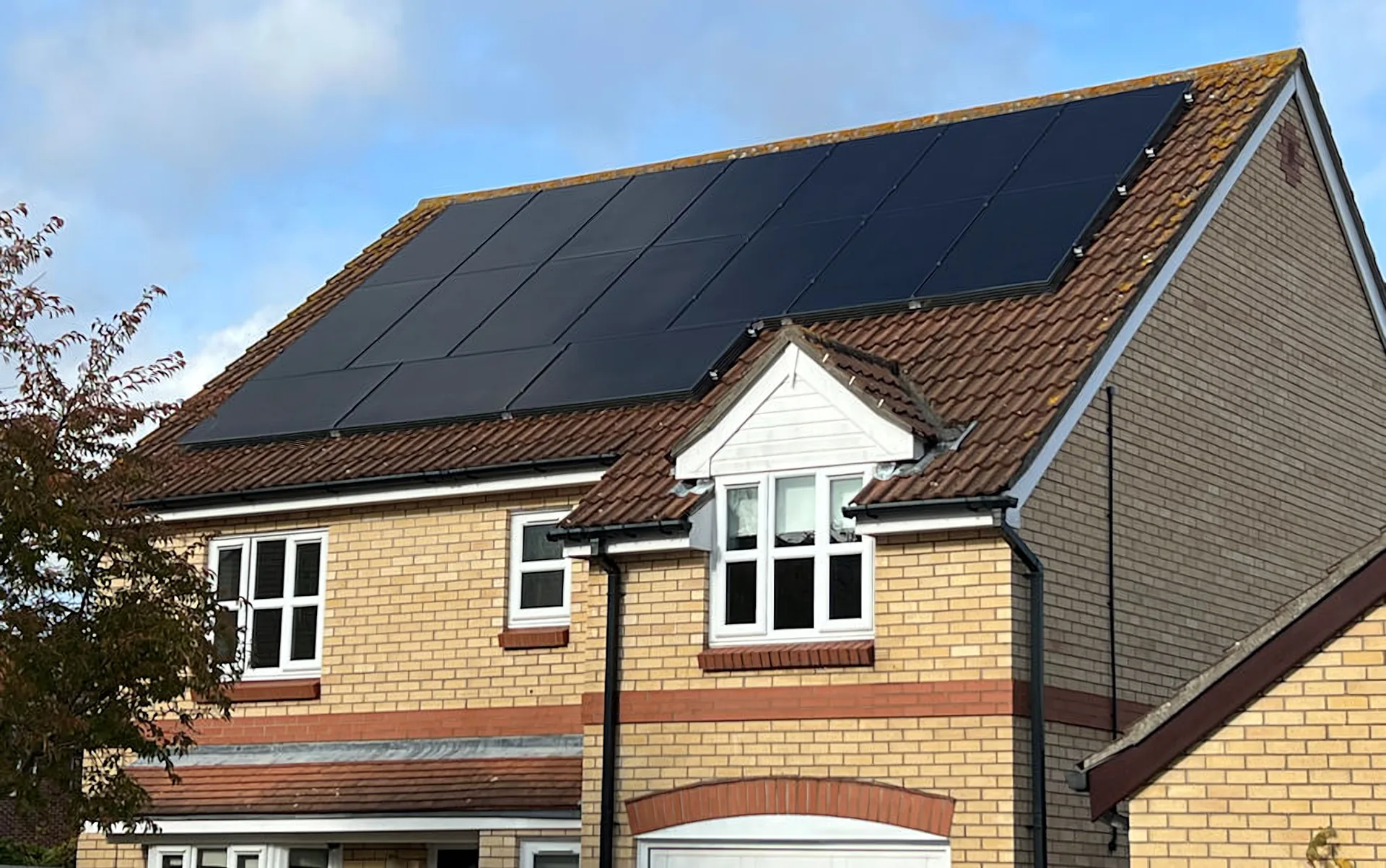 All-black solar panels on the tiled roof of a yellow-brick family home in England