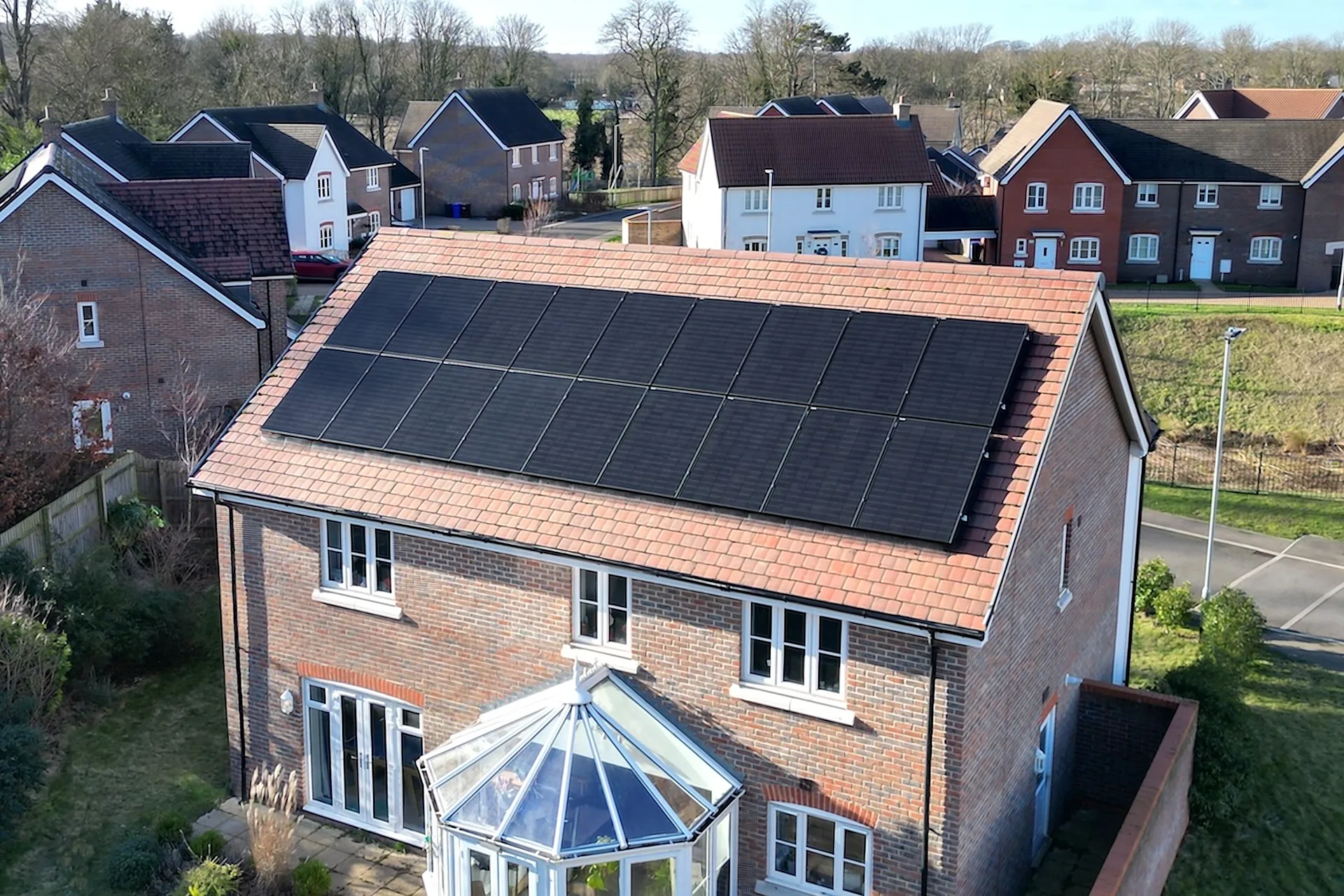 Aerial view of a red-brick UK detached home with a full array of black solar panels on a tiled roof